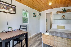 A room with a dining table, chairs, a bed with a wicker headboard, a ceiling fan, and a framed picture on the wall. - Tiny House Experience in Las Vegas w/ Free Parking (Las Vegas)