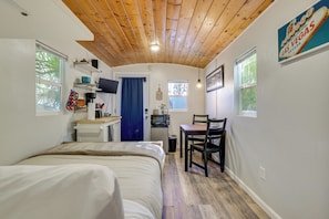 A compact room with a bed, a small desk, a chair, a microwave, and a window with a blue curtain. - Tiny House Experience in Las Vegas w/ Free Parking (Las Vegas)