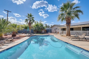 A swimming pool with lounge chairs, palm trees, and a white picket fence.