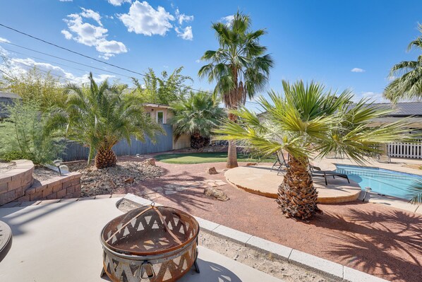 Un jardin avec une piscine, des palmiers, un barbecue et un espace patio.