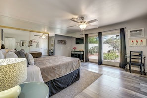 A bedroom with a bed, ceiling fan, large window, and a view of the outdoors.