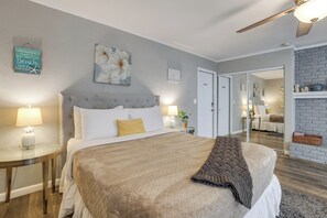 Ein Schlafzimmer mit einem Bett, Nachttischen, einem Deckenventilator und Blick in einen anderen Raum.