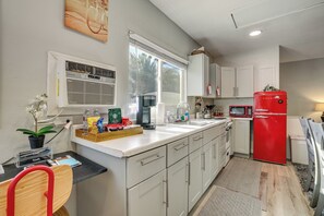 A modern kitchen with white cabinets, a red refrigerator, a window with blinds, and a countertop with various items. - Free Parking! Vegas Studio Near Strip & Airport (Las Vegas)