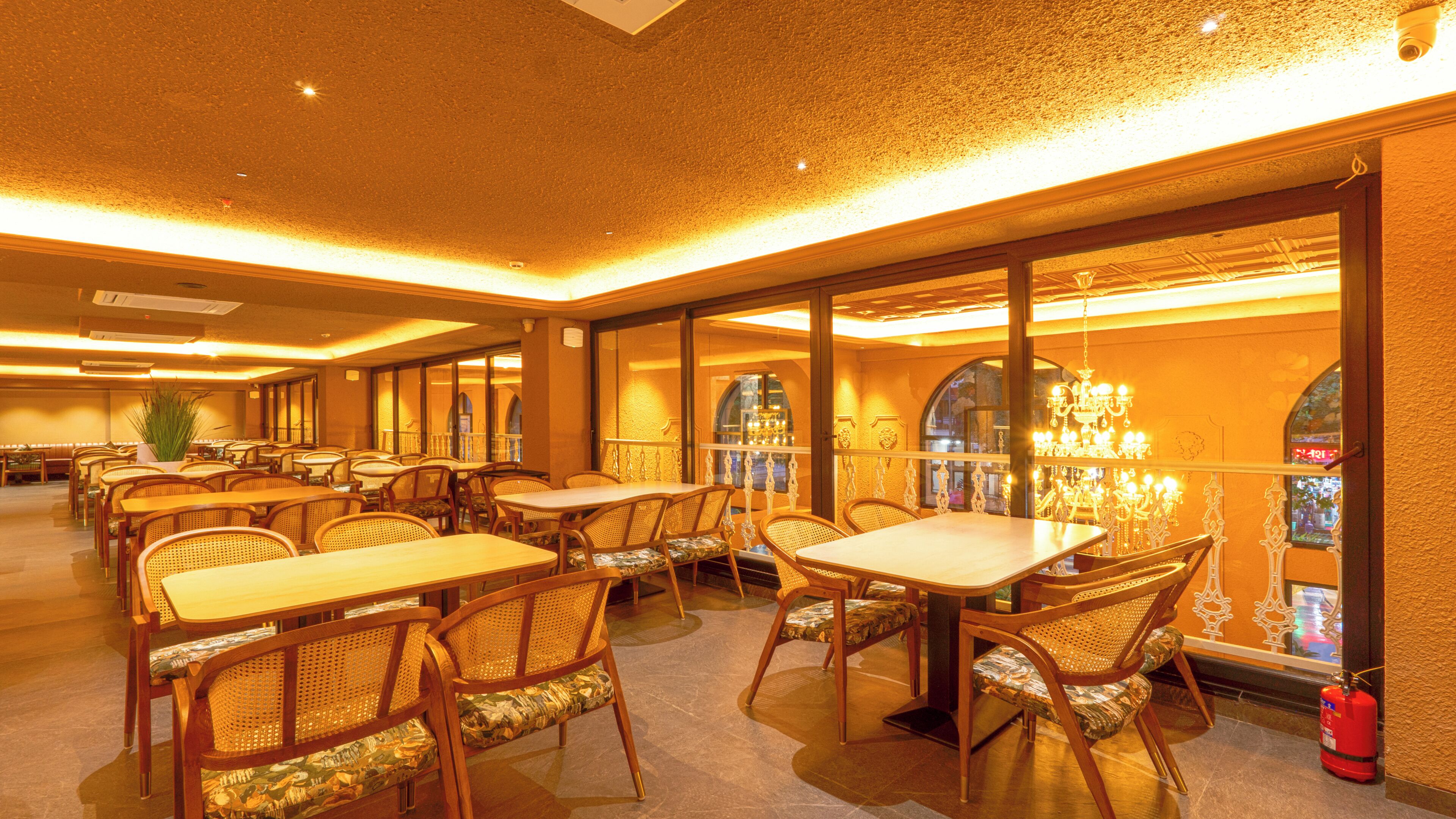 A restaurant with multiple tables and chairs, large windows, and a chandelier.