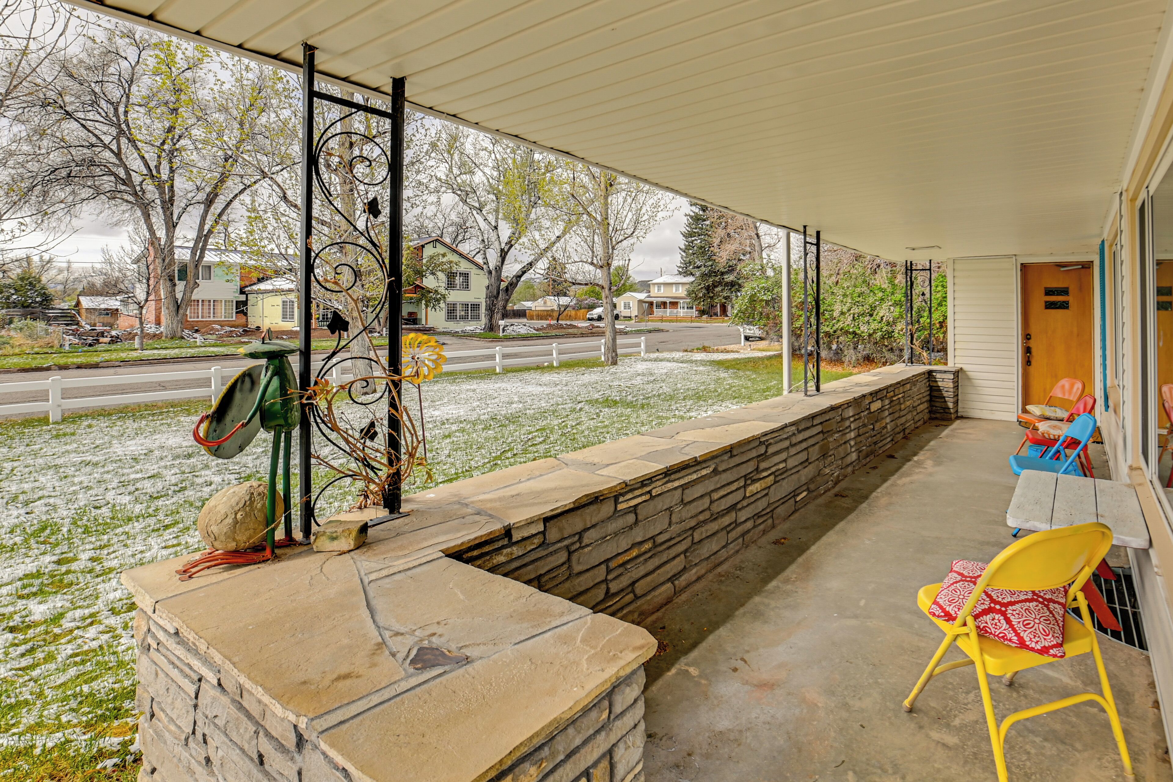 A covered porch with a stone wall, a yellow chair, and a view of a street with houses.