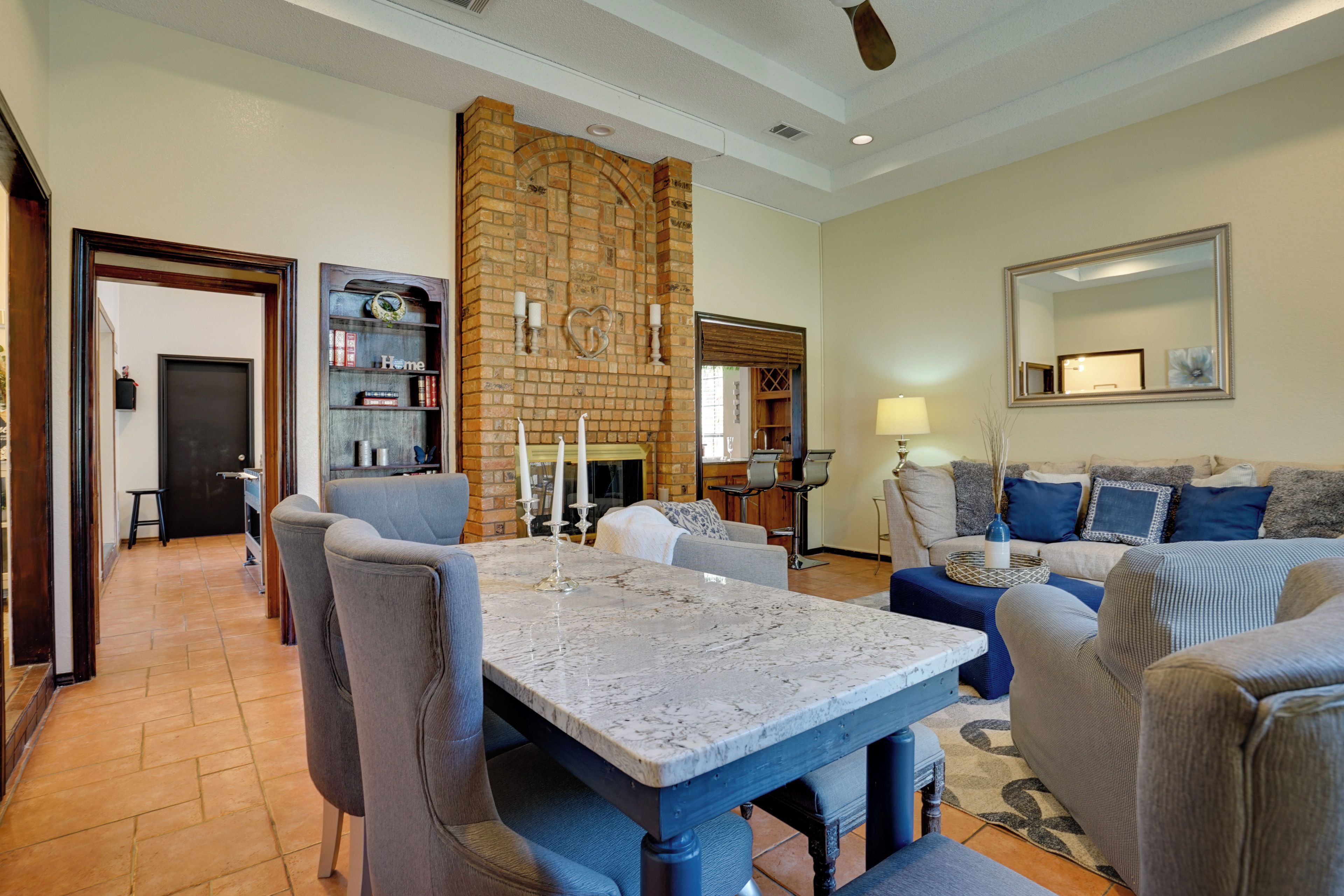 Uma sala de estar com lareira de pedra, sala de jantar com mesa de mármore e área de estar com sofá e poltronas.