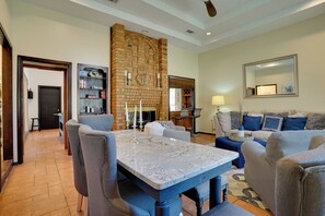 Uma sala de estar com lareira de pedra, sala de jantar com mesa de mármore e área de estar com sofá e poltronas.