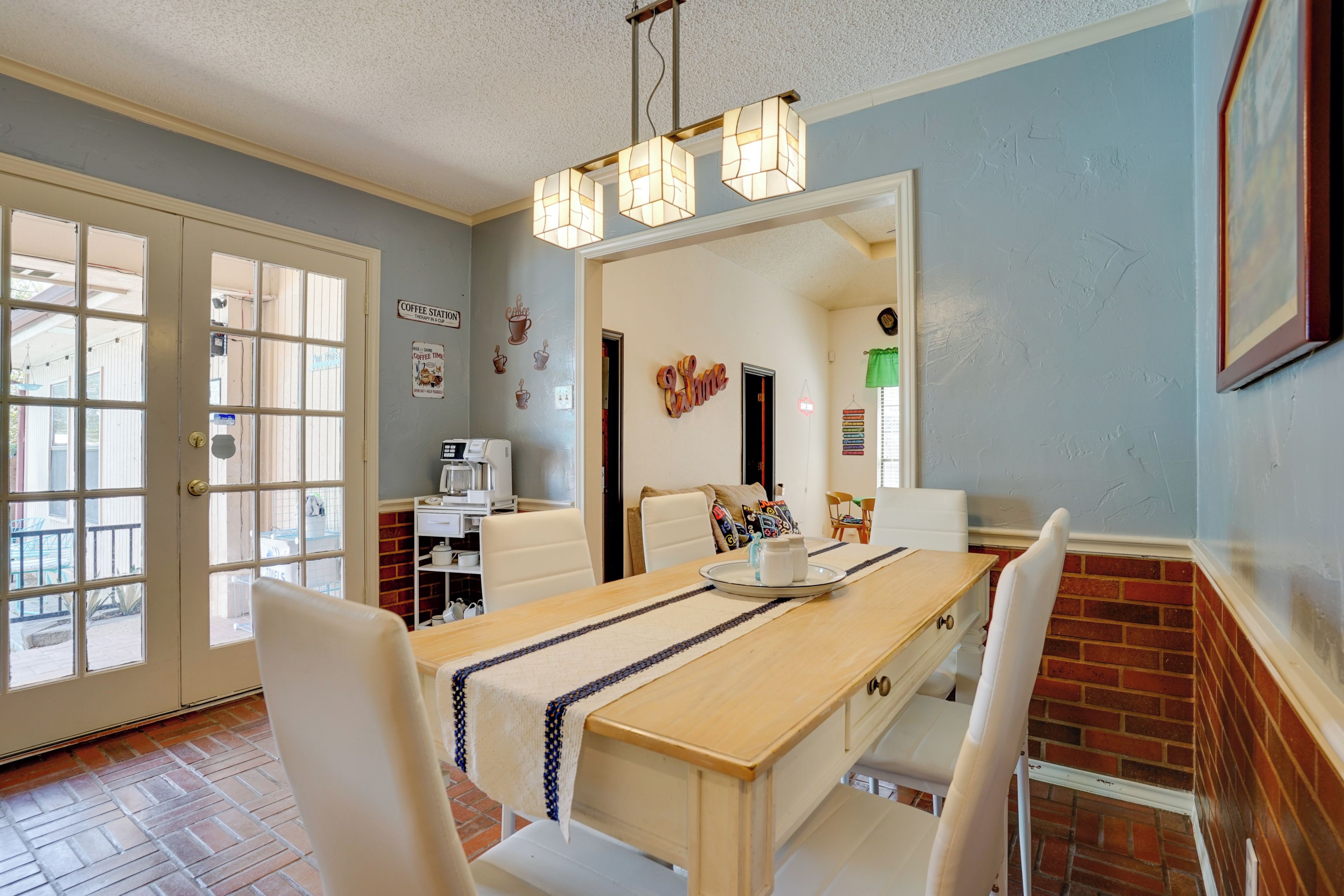 A dining area with a long table, white chairs, a coffee station, and a brick wall.