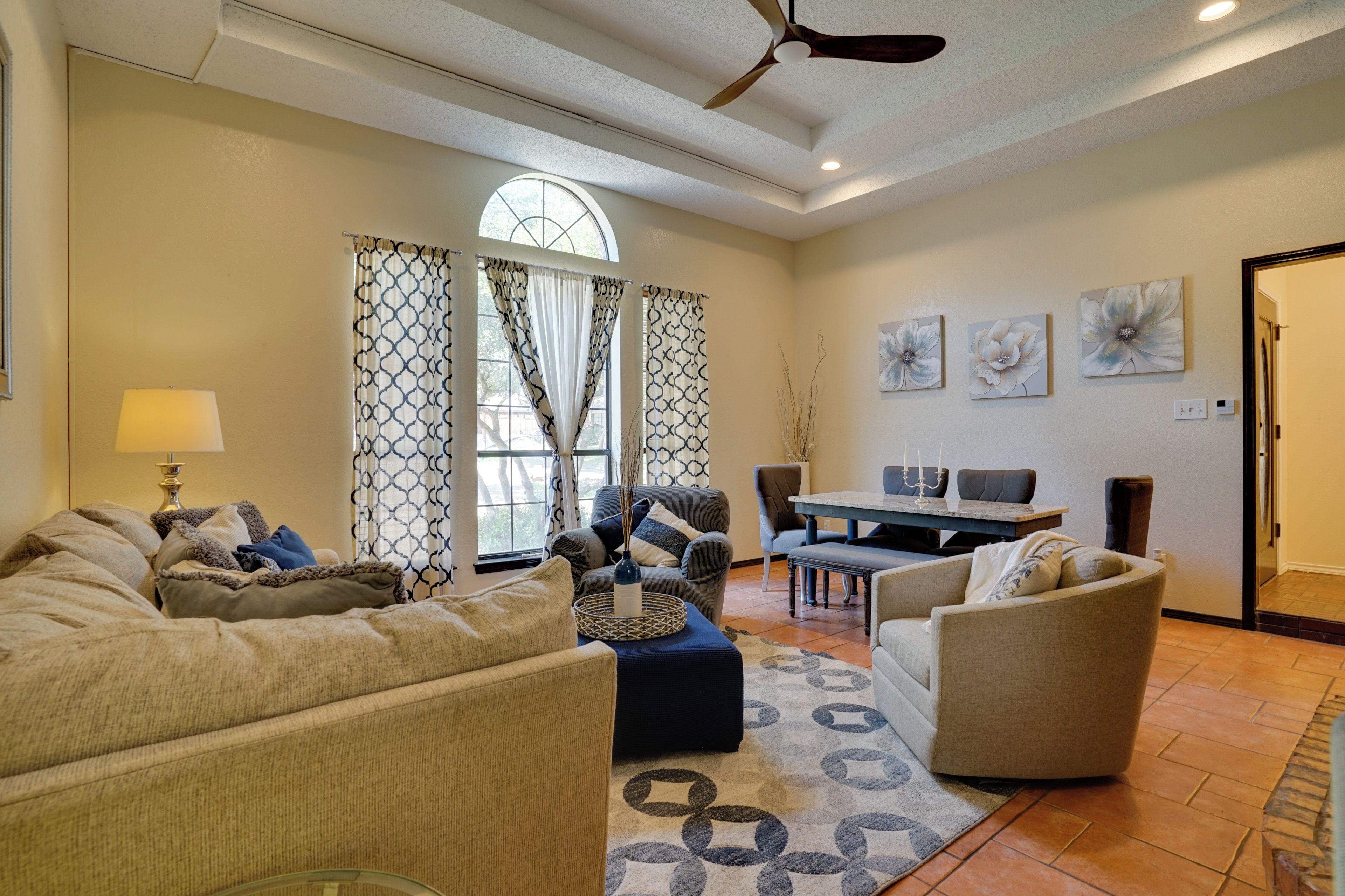 A spacious living room with a large window, a ceiling fan, and a dining area with a table and chairs.