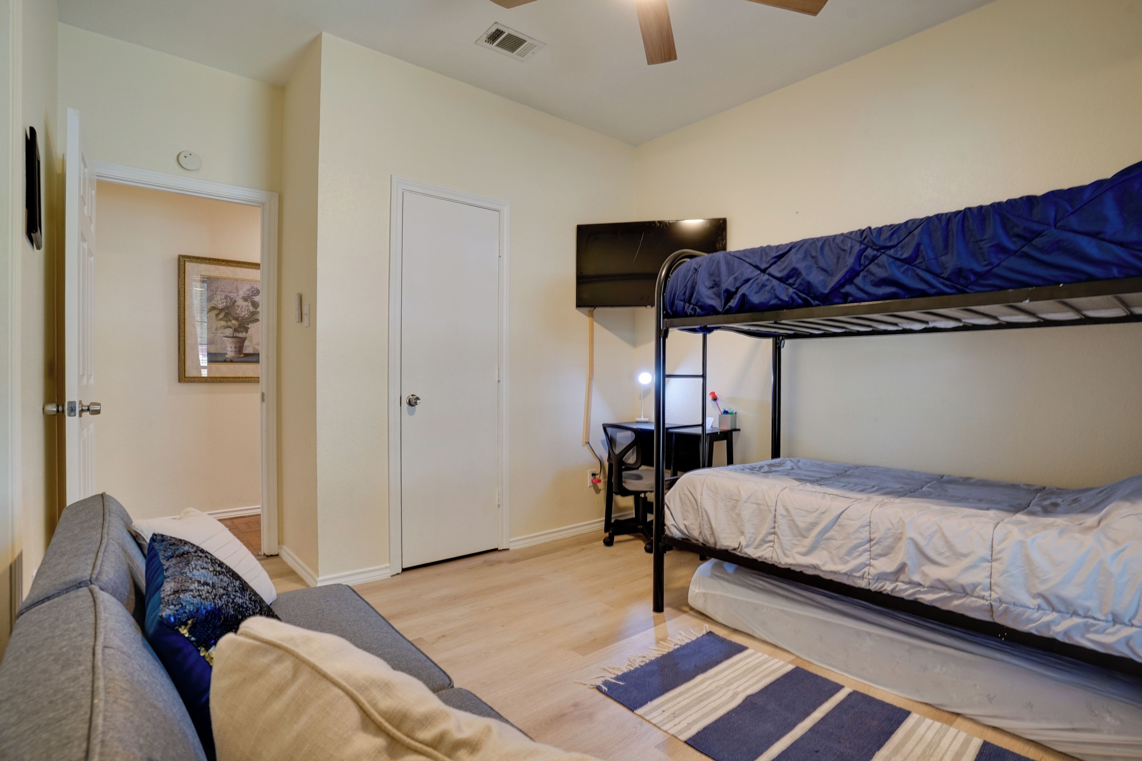 A bedroom with a bunk bed, a desk, a chair, a sofa, and a door.