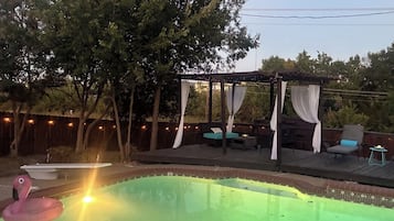Um quintal com piscina, deck de madeira e área de estar coberta.