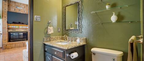 A bathroom with a granite countertop sink, a toilet, and a glass shelf with toiletries.
