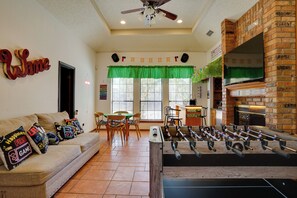 A cozy living room with a fireplace, a foosball table, and a green window valance. - 3 Mi to Six Flags! Family Getaway w/ Outdoor Oasis (Grand Prairie)