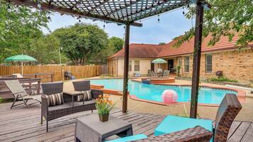 Um quintal com deck de madeira, móveis de exterior, piscina e pérgola.