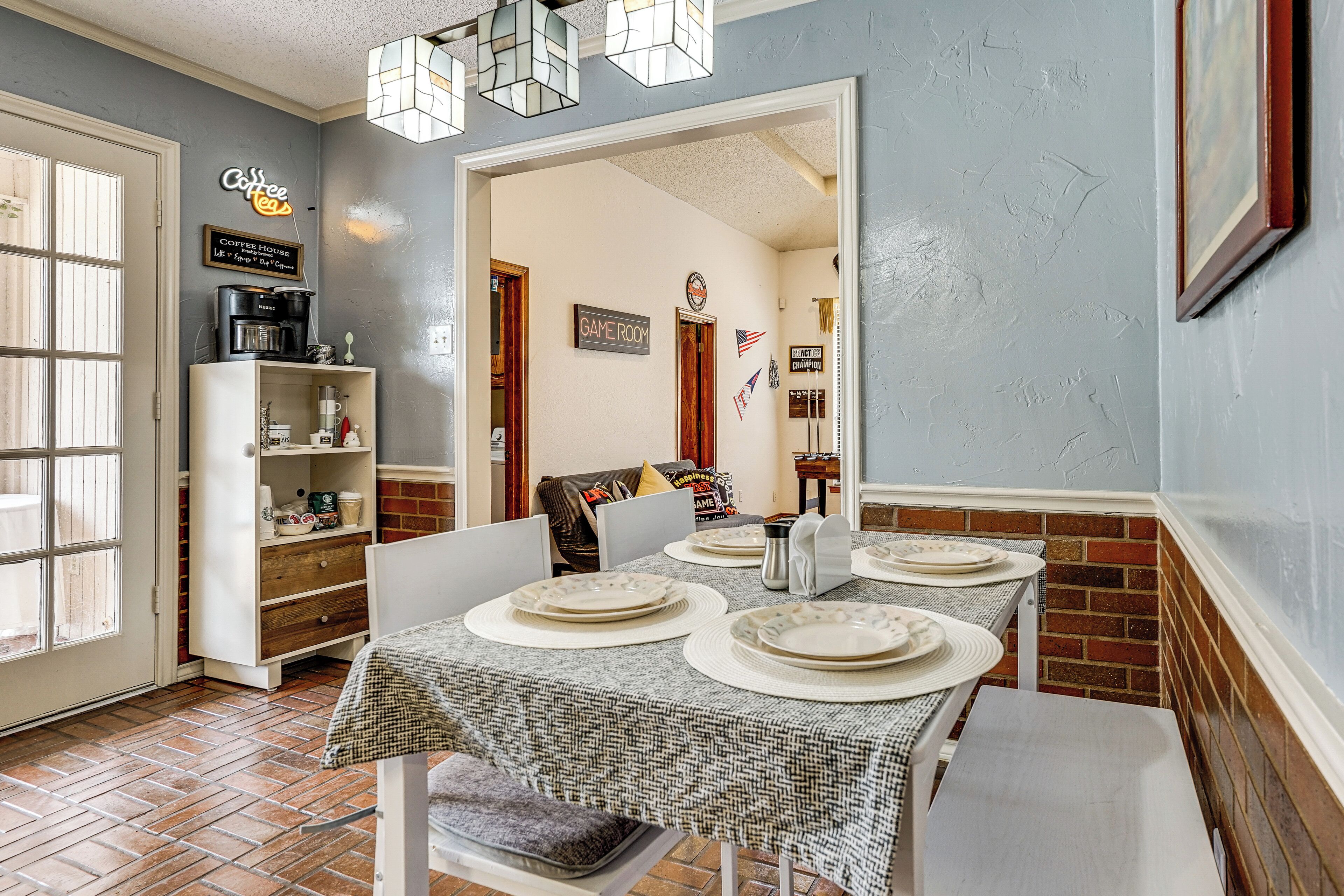 Uma área de refeições com uma mesa posta para quatro pessoas, um espaço para café e uma placa indicando a sala de jogos.