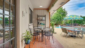 A patio area with a round table and chairs, a small shelf with books, and a pool in the background. - 3 Mi to Six Flags! Family Getaway w/ Outdoor Oasis (Grand Prairie)
