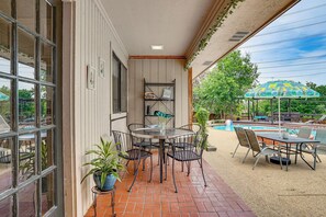 A patio area with a round table and chairs, a small shelf with books, and a pool in the background. - 3 Mi to Six Flags! Family Getaway w/ Outdoor Oasis (Grand Prairie)