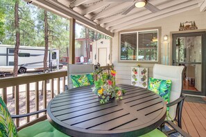 Eine überdachte Terrasse im Freien mit einem runden Tisch, Stühlen und einem Vogelkäfig mit Blumen.