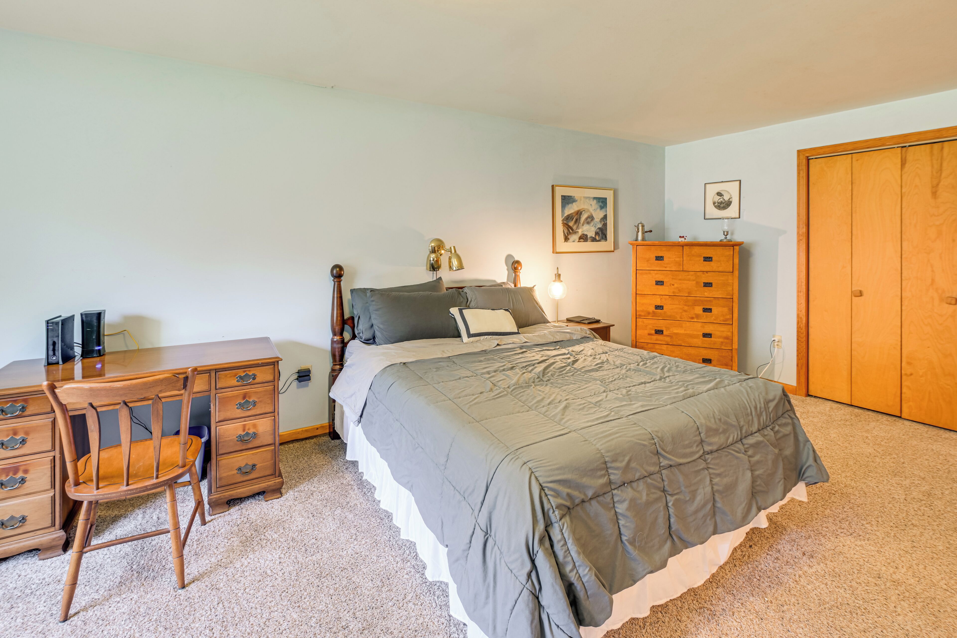 A bedroom with a bed, a wooden dresser, a desk, and a wardrobe.