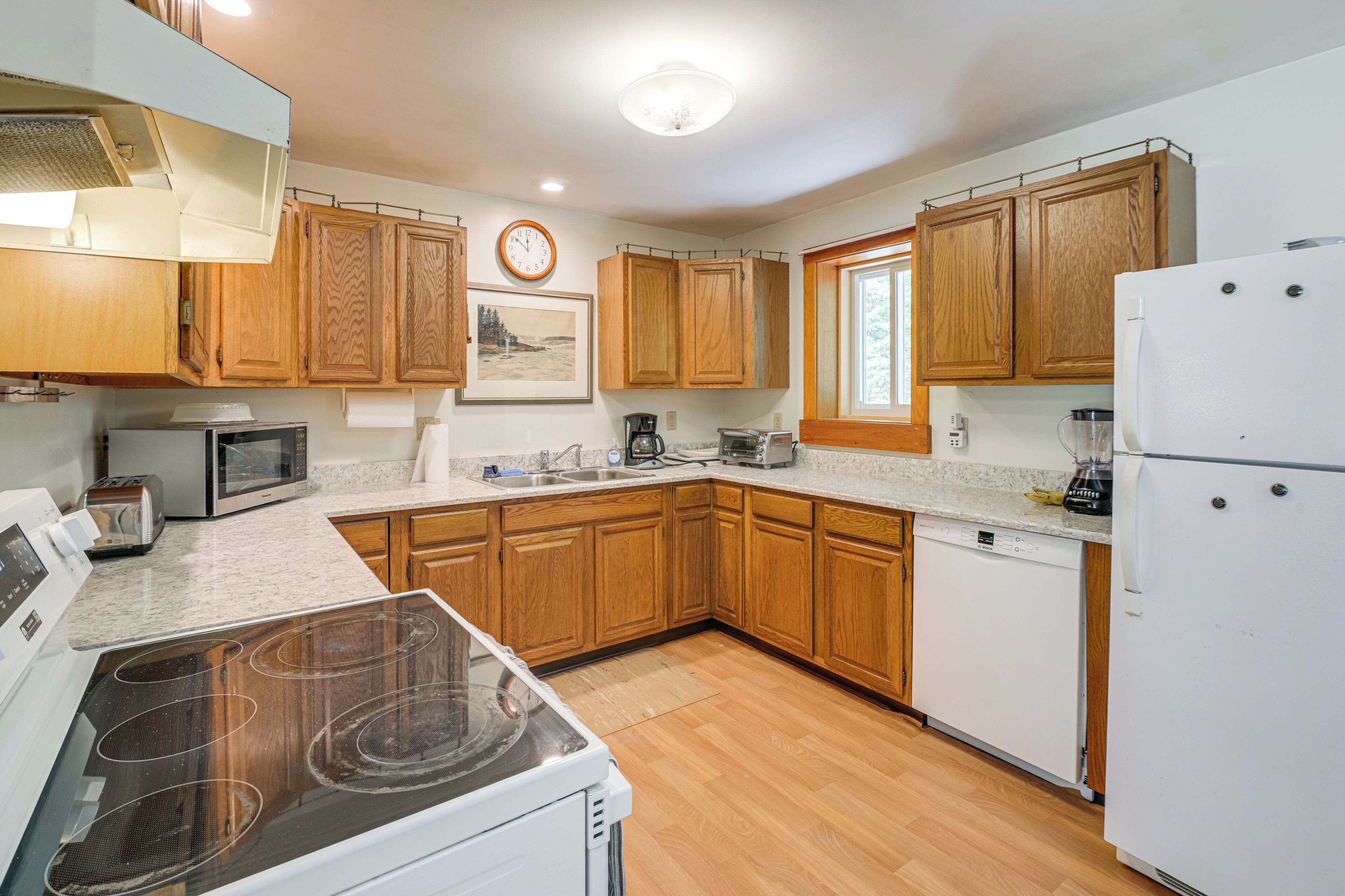 A kitchen with wooden cabinets, a microwave, a toaster, a stove, a dishwasher, and a refrigerator.