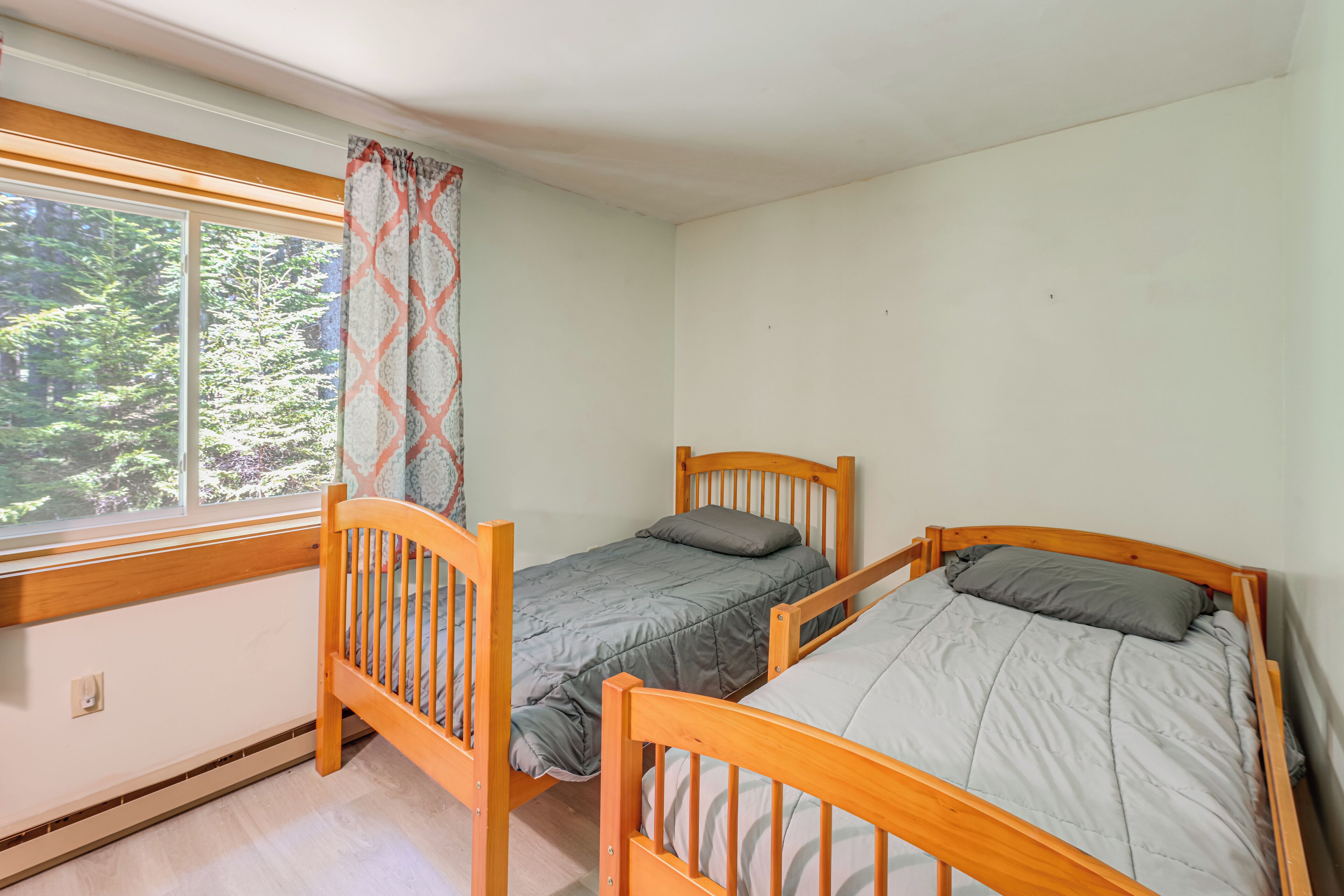 A room with two wooden beds, a window with a view of trees, and a curtain.