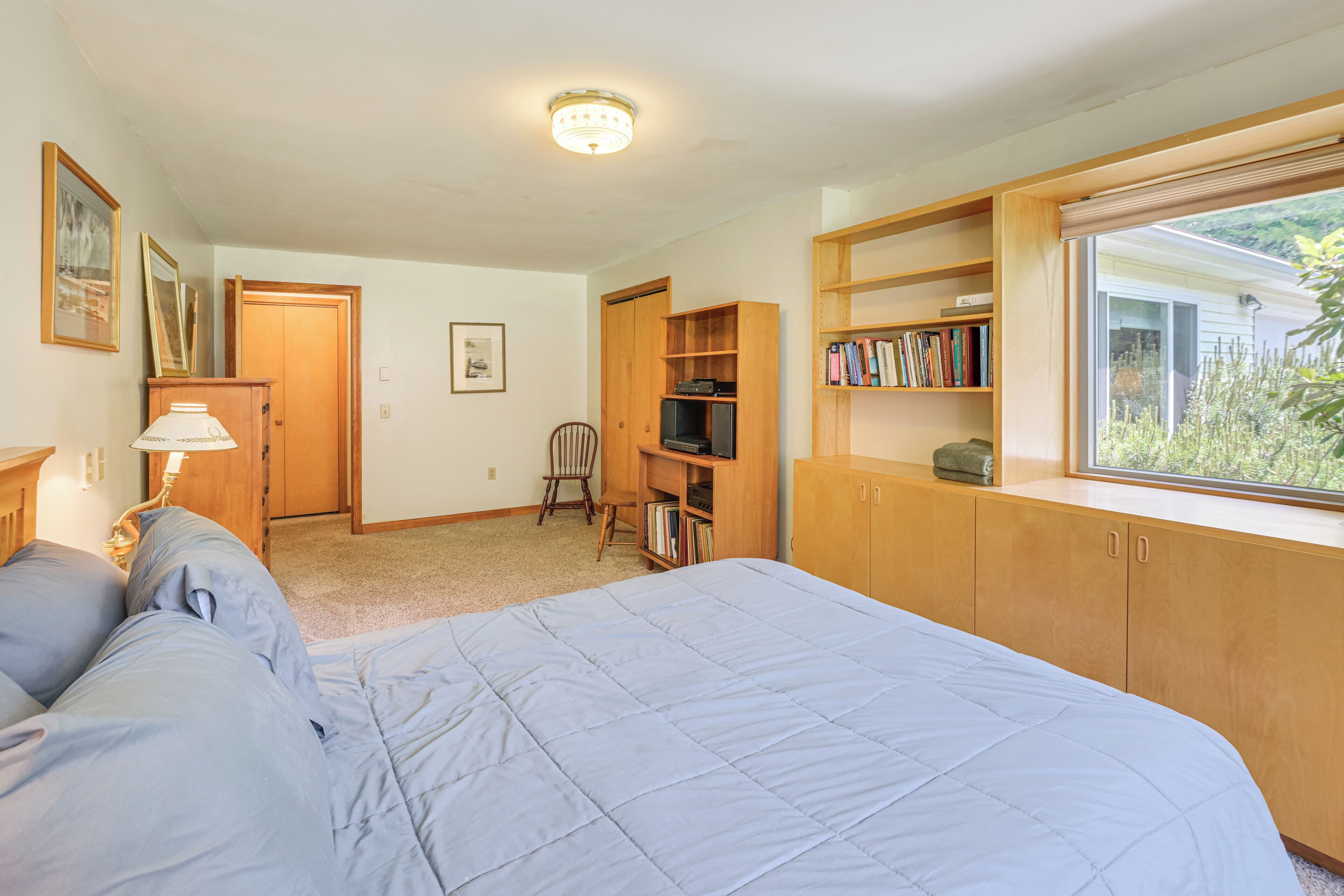 A bedroom with a bed, a desk, a chair, a bookshelf, and a window.