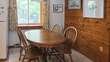 A wooden-paneled room with a round dining table, chairs, a refrigerator, and a window with curtains.