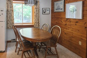 A wooden-paneled room with a round dining table, chairs, a refrigerator, and a window with curtains. - Kenway Ranch: Family Retreat Near Acadia Trails (Southwest Harbor)