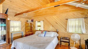 A wooden-paneled room with a bed, a desk, a fan, and a fireplace. - Waterfront Berkshires Studio w/ Dock on Goose Pond (Lee)