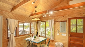 A wooden cabin interior with a dining table, chairs, a ceiling fan, and a view of the outdoors. - Waterfront Berkshires Studio w/ Dock on Goose Pond (Lee)