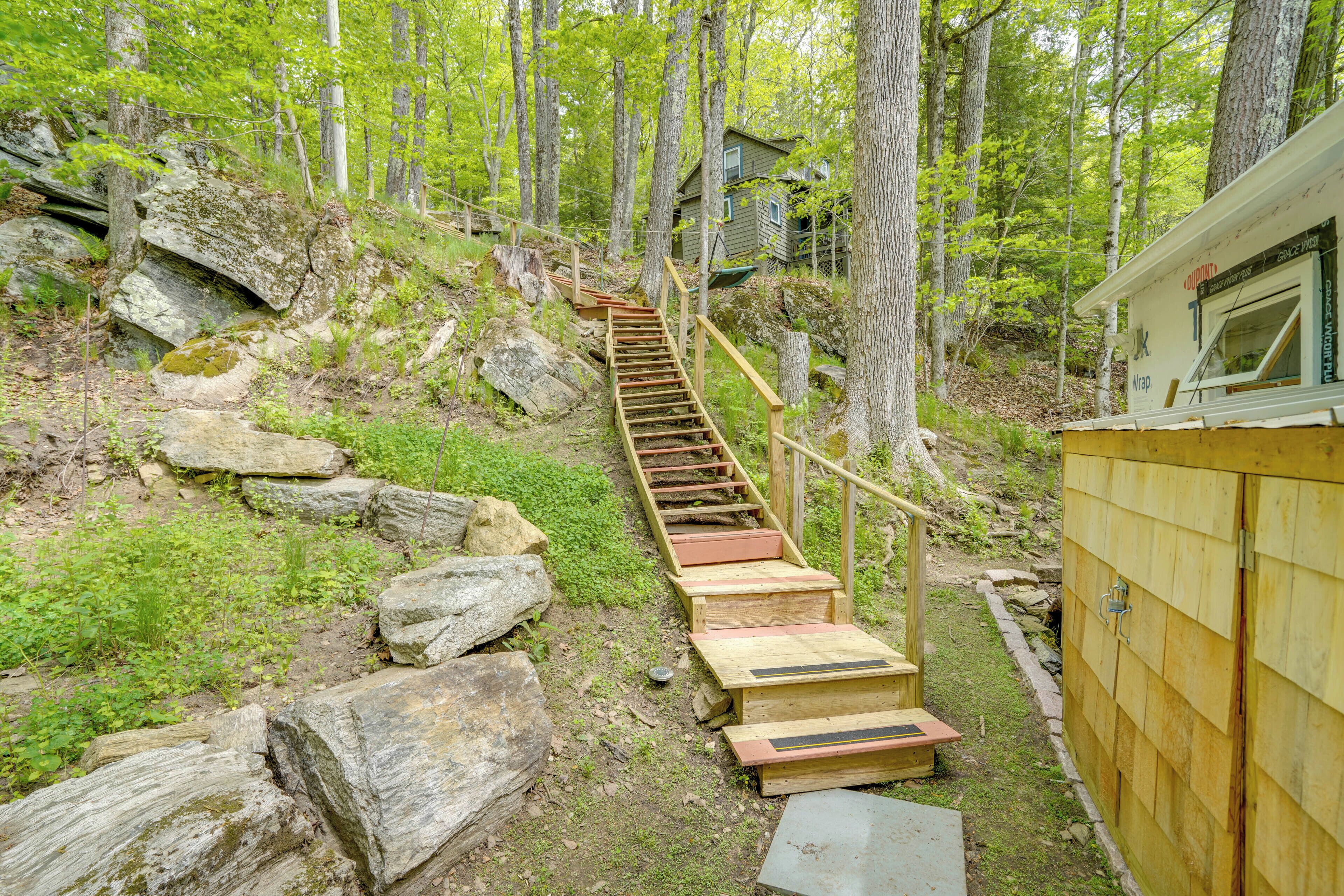 A wooden staircase leading to a cabin in a forested area with large rocks and greenery.