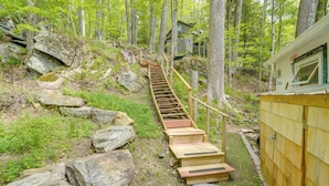 A wooden staircase leading to a cabin in a forested area with large rocks and greenery. - Waterfront Berkshires Studio w/ Dock on Goose Pond (Lee)