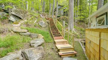 A wooden staircase leading to a cabin in a forested area with large rocks and greenery.