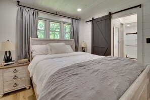 Ein Schlafzimmer mit einem Bett, zwei Nachttischen, einem Fenster mit Vorhängen, einer Schiebetür im Scheunenstil und einem Beistelltisch mit einer Lampe.