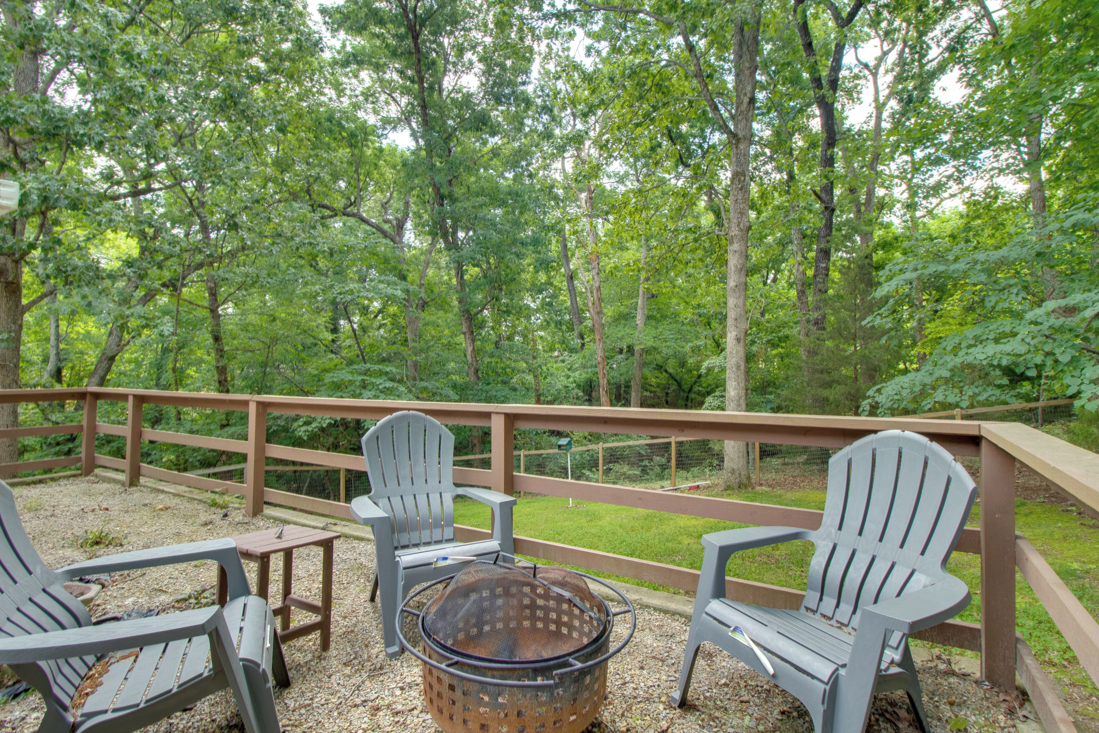 Eine Terrasse mit Adirondack-Stühlen, einer Feuerstelle und Blick auf ein bewaldetes Gebiet.