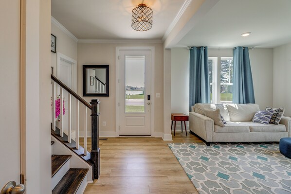 A hallway with a wooden staircase, a white door, a sofa, and a patterned rug.