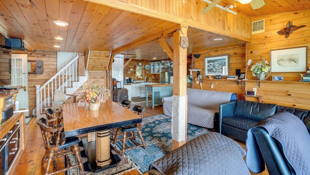 A log cabin interior with a dining area, sofa, kitchen, and staircase. - Lakeside Berkshires Cabin w/ Private Dock & Views (Lee)