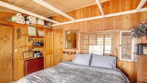 A wooden room with a bed, a dresser, a shelf with toiletries, and a window. - Lakeside Berkshires Cabin w/ Private Dock & Views (Lee)