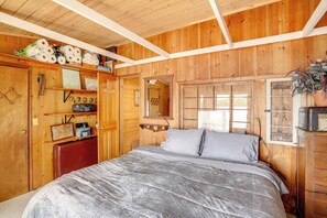 A wooden room with a bed, a dresser, a shelf with toiletries, and a window.
