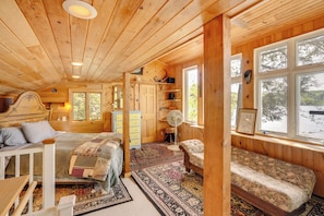 L’intérieur d’un chalet accueillant, avec un lit, un banc, une commode et une fenêtre donnant sur les arbres.