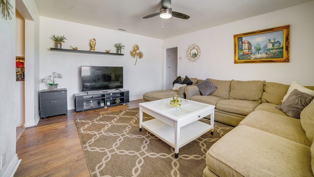 A living room with a sofa, TV, coffee table, ceiling fan, decorative items, and artwork. - Commuter Friendly! Extended Stay in Riverside (Riverside)