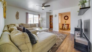A living room with a sofa, coffee table, and TV stand. There is a ceiling fan, a plant on a shelf, and a dining area in the background. - Commuter Friendly! Extended Stay in Riverside (Riverside)