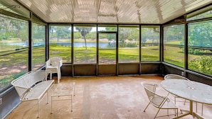 Une terrasse couverte avec vue sur un lac, des chaises en métal et une table.