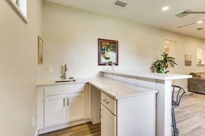 A modern kitchen with white cabinetry, a countertop island, and a dining area with a chair.