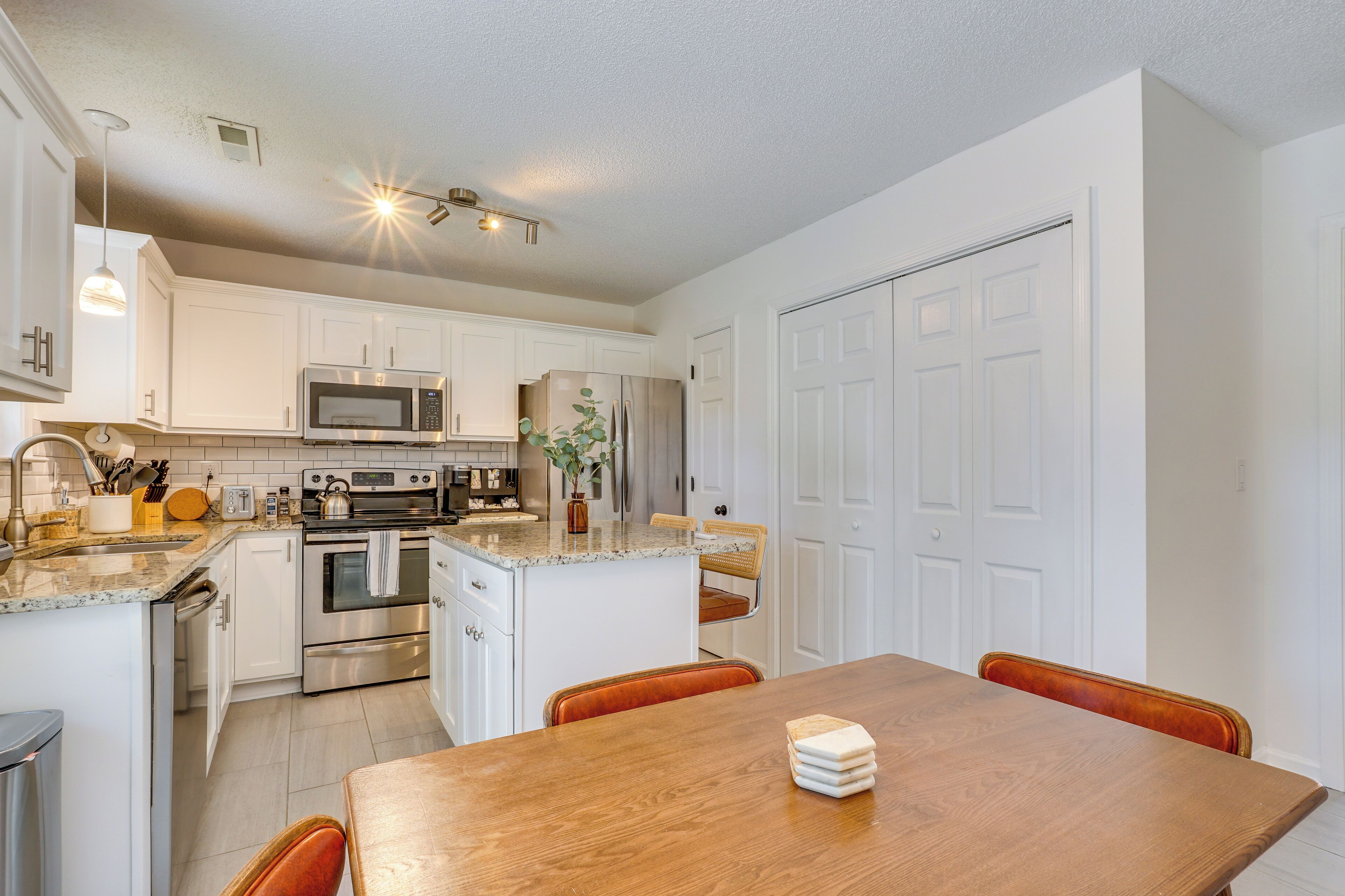 Una cocina moderna con armarios blancos, electrodomésticos de acero inoxidable y una mesa de comedor de madera.