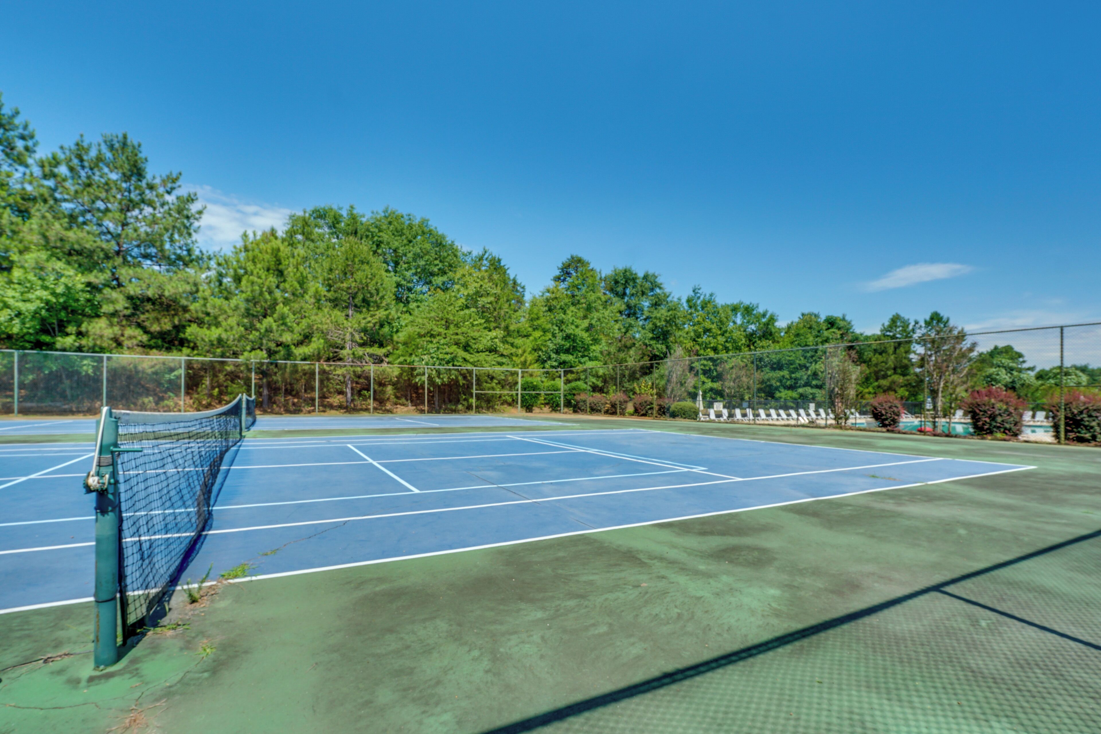 An outdoor tennis court with a net, surrounded by trees and a fence.