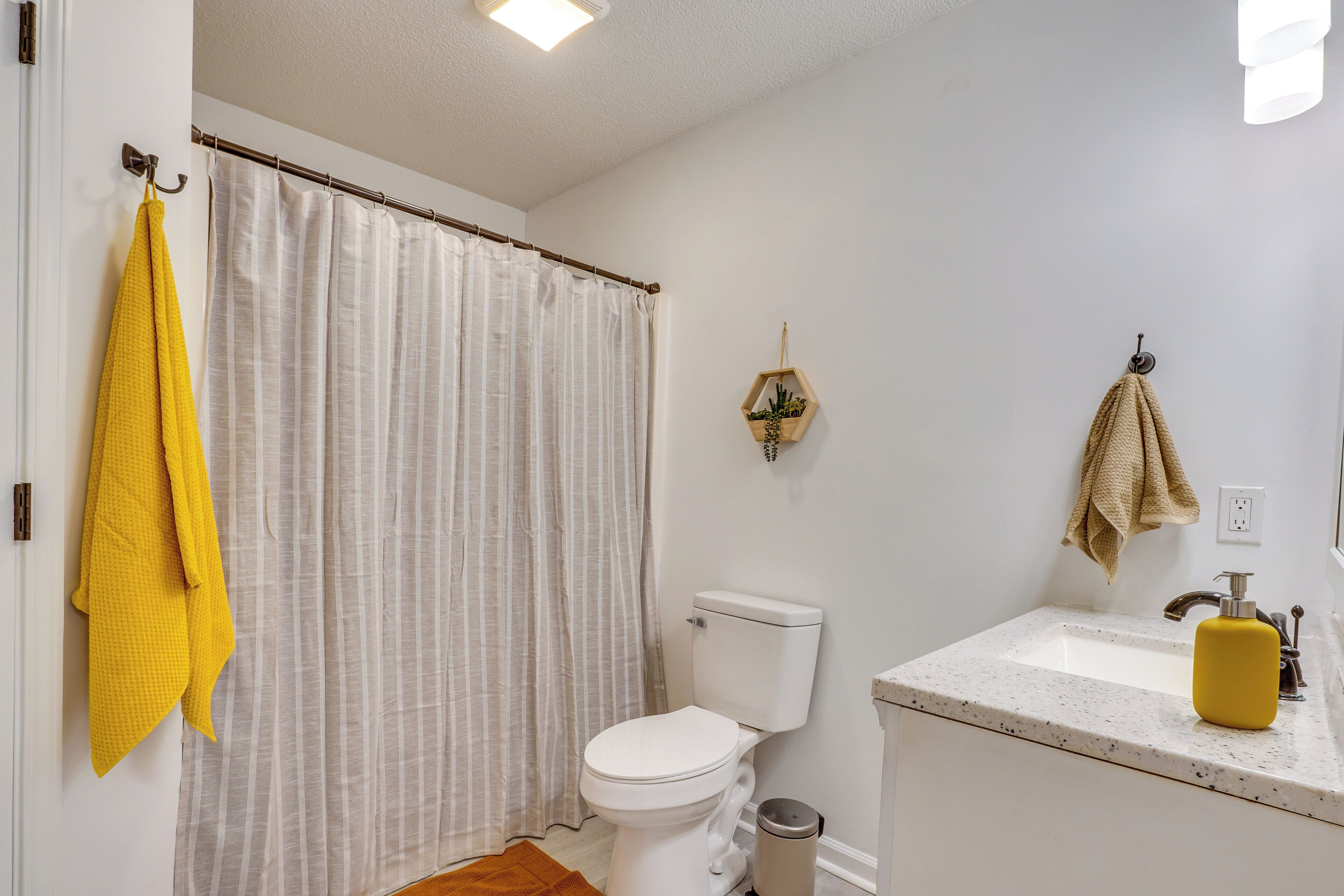 Un baño con inodoro, lavabo, cortina de ducha y una toalla amarilla.
