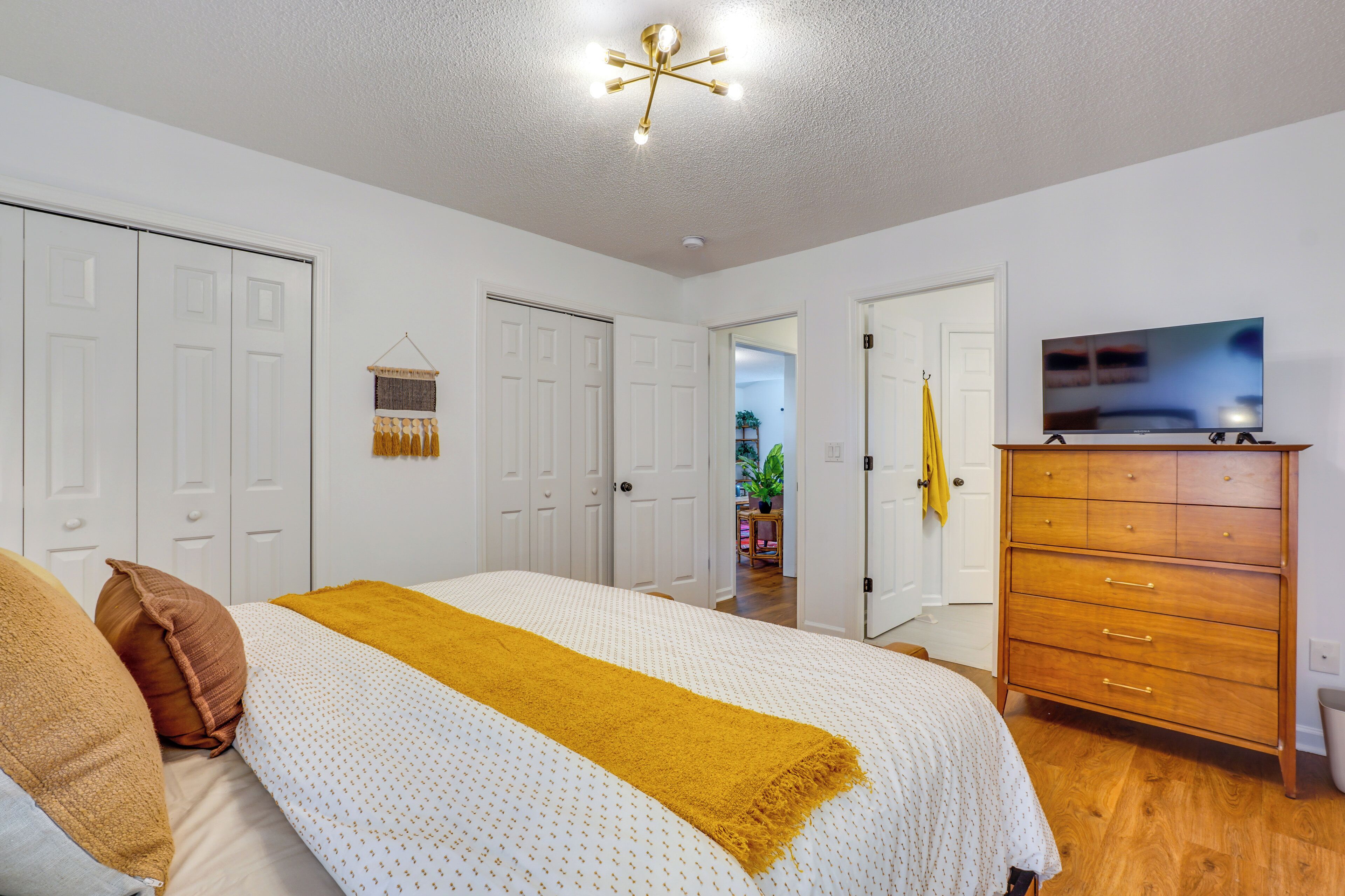 A bedroom with a bed, a dresser, a television, and a hallway leading to another room.