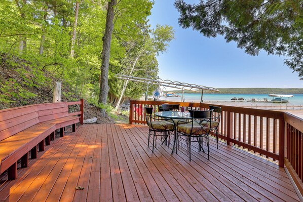 A wooden deck with a table and chairs, overlooking a beach and the sea.