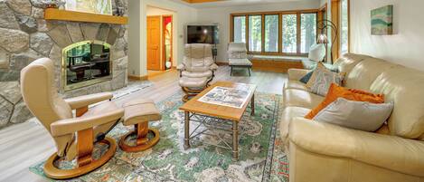 A spacious living room with a stone wall, a fireplace, leather furniture, and large windows.